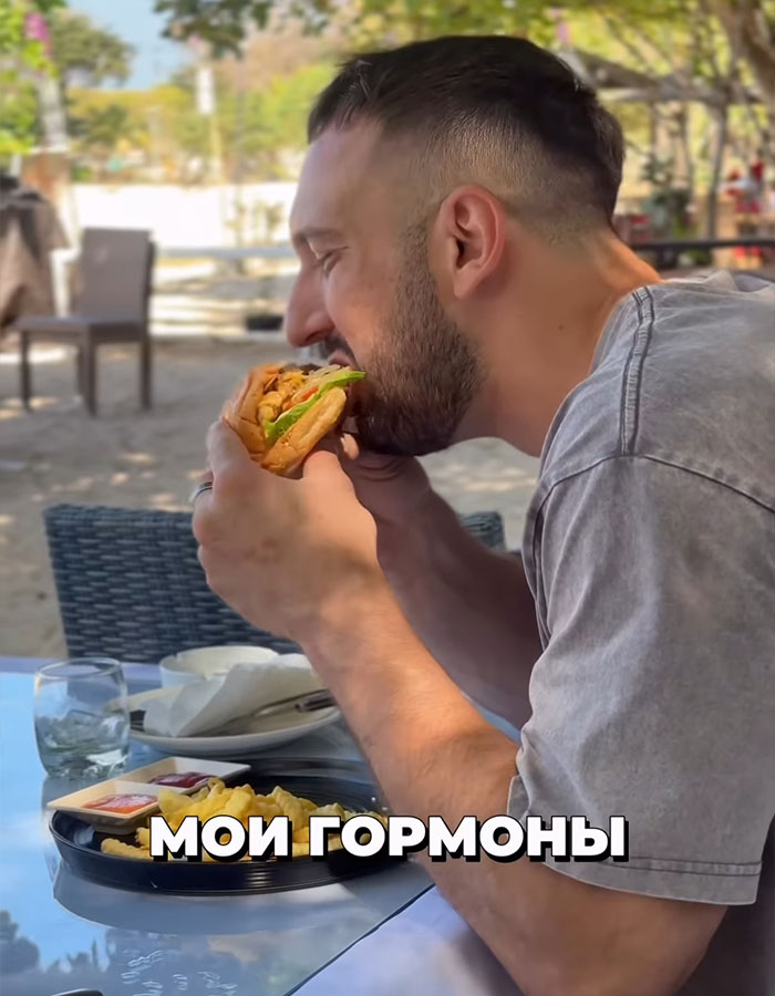 Man biting into a sandwich outdoors, illustrating a binge-eating challenge related to a fitness coach and mayo consumption.