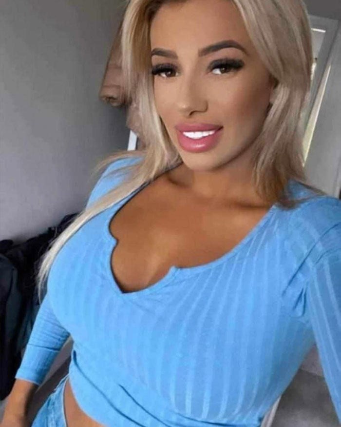 Blonde woman in a blue top smiling in a selfie, representing women who had a BBL and faced tragic consequences.