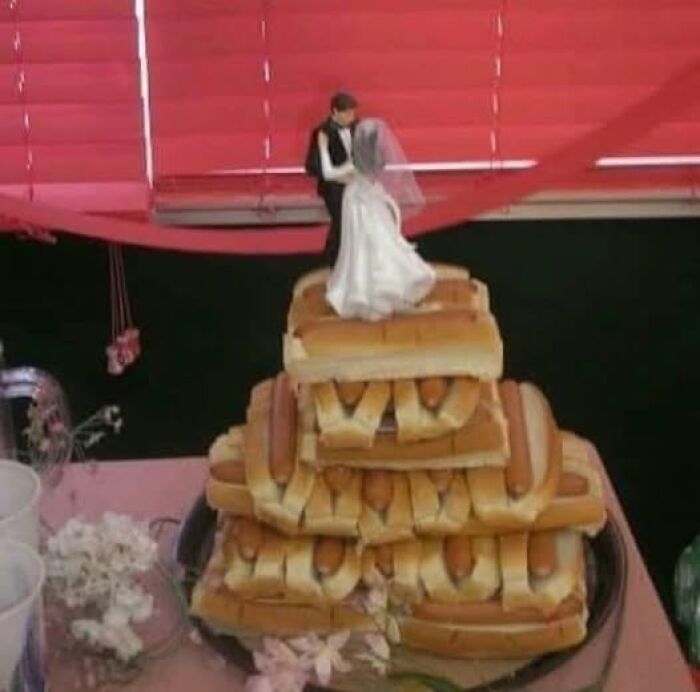 Bride and groom figurines on a pyramid of hot dog sandwiches, an unusual and hard-hitting wedding cake display.