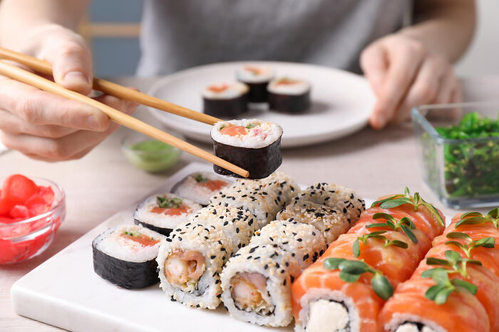 Person holding chopsticks picking sushi roll, illustrating lovable things clueless dads did during pregnancy.