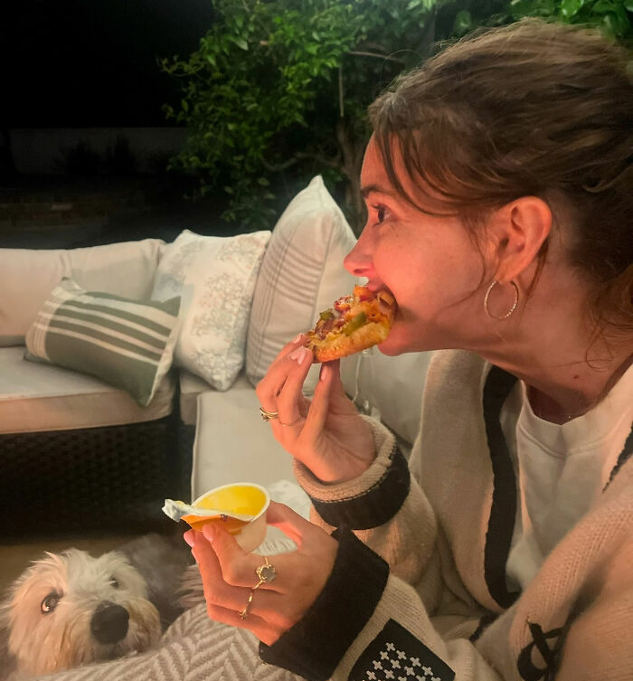 Woman eating pizza on outdoor couch at night with dog nearby, highlighting influencer behavior amid contagious infection concerns. Woman eating pizza on outdoor couch at night with dog nearby, highlighting influencer behavior amid contagious infection concerns.