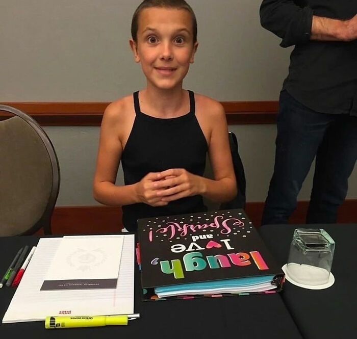 Millie Bobby Brown sitting at a table with a colorful notebook, highlighting bullying issues faced by the Stranger Things star.