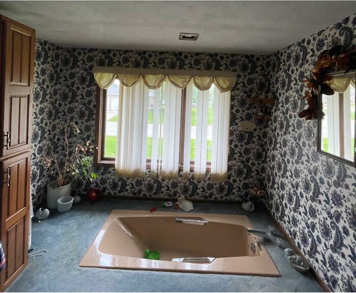 Vintage bathroom with sunken bathtub, floral wallpaper, and window curtains in a unique Zillow home interior design.