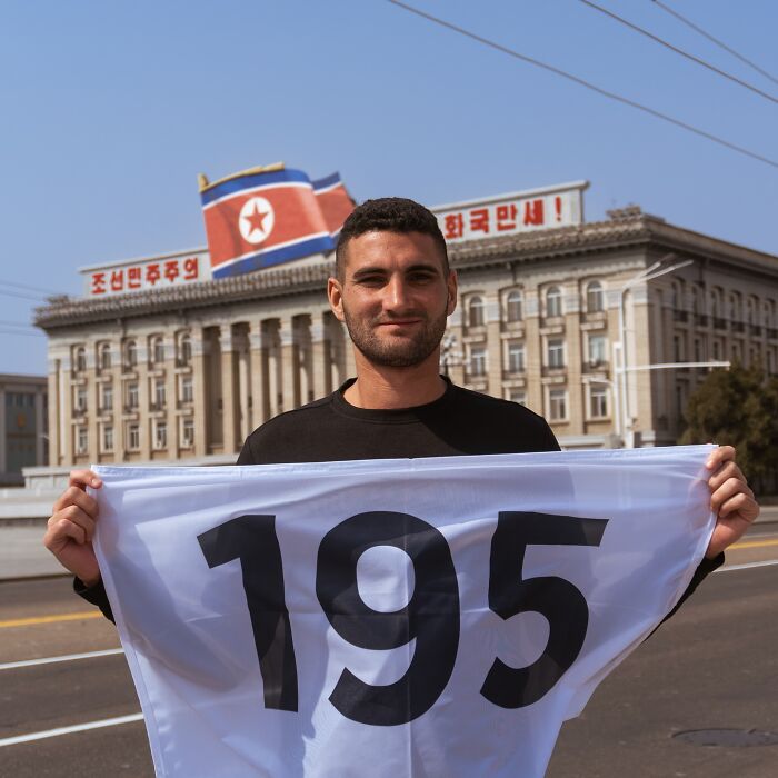 American travel influencer holding marathon bib 195 in North Korea with a flag and building in background.