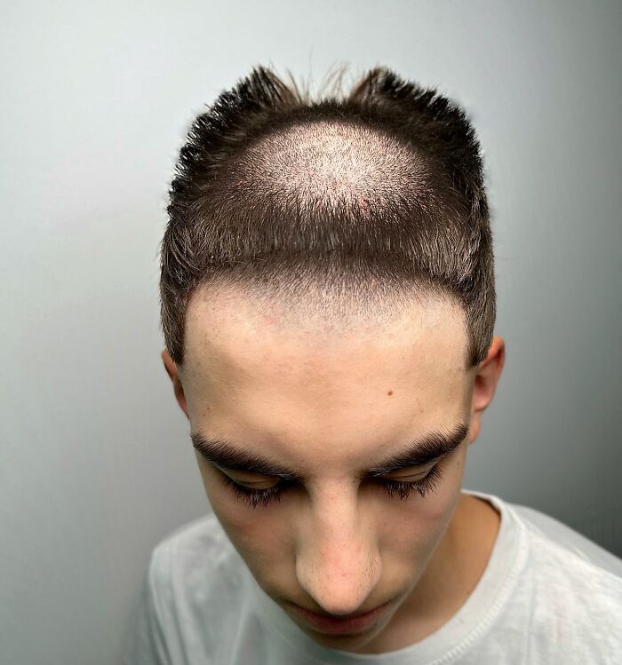 Young man with a bold barber haircut featuring sharp edges and a high fade smiling against a plain background