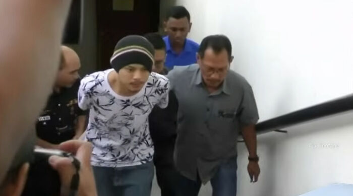 Man in a beanie and floral shirt escorted by authorities, related to body of provocative influencer found in hotel bathtub case. Man in a beanie and floral shirt escorted by authorities, related to body of provocative influencer found in hotel bathtub case.