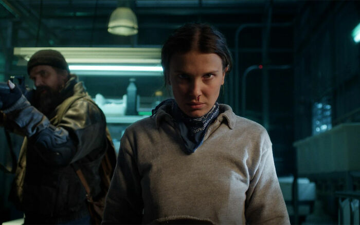 Millie Bobby Brown looking intense in dimly lit room, breaking silence about adopting a baby at 21 after criticism. Millie Bobby Brown looking intense in dimly lit room, breaking silence about adopting a baby at 21 after criticism.