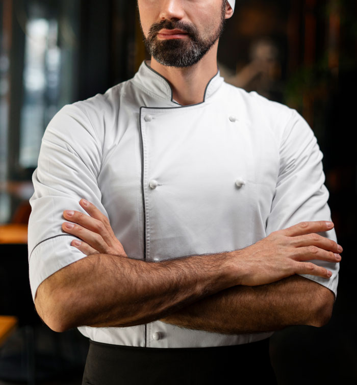 Bearded chef in white uniform with crossed arms showcasing confidence in a restaurant setting, capturing instant karma moment.