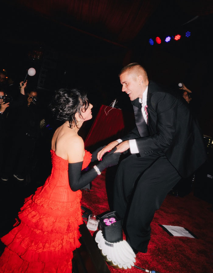 A woman in a red dress and black gloves interacting with a man in a tuxedo at Kris Jenner's 70th birthday bash.