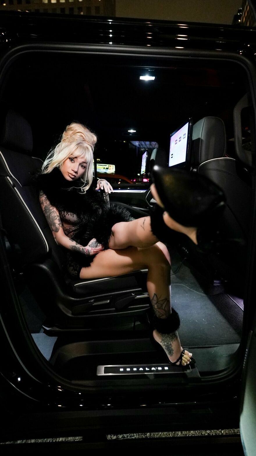 Bhad Bhabie posing confidently inside a luxury vehicle showing stylish tattoos and glamorous fashion at night.