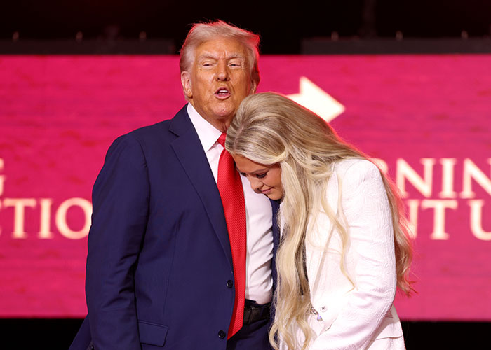 Man in suit and red tie speaking while a woman with long blonde hair leans in, gestures hint at expressive acting and emotions.