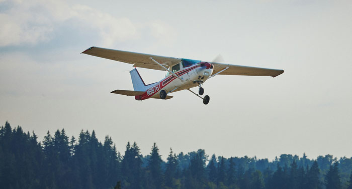 Small single-engine airplane flying low above forested area, illustrating pilots' mid-flight close calls in aviation.