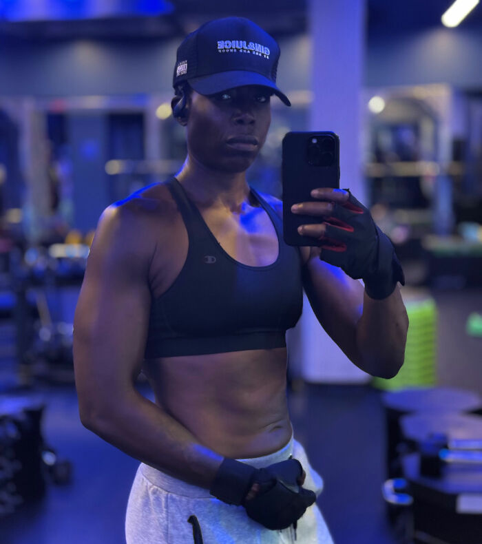 Muscular person wearing gloves and a cap taking a mirror selfie at the gym amid Gold's Gym trans locker controversy discussion. Muscular person wearing gloves and a cap taking a mirror selfie at the gym amid Gold's Gym trans locker controversy discussion.