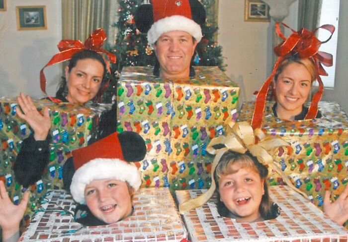Five people dressed as wrapped presents with bows and Santa hats in an awkward studio photo during Christmas time.