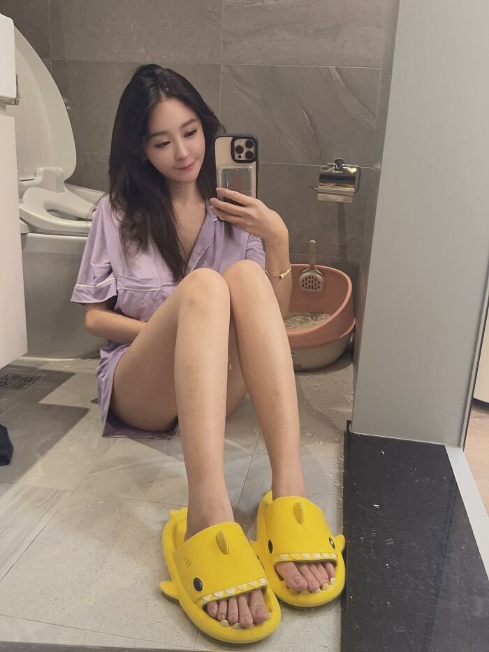Young woman taking a mirror selfie sitting on bathroom floor wearing yellow slippers, related to provocative influencer and hotel bathtub. Young woman taking a mirror selfie sitting on bathroom floor wearing yellow slippers, related to provocative influencer and hotel bathtub.