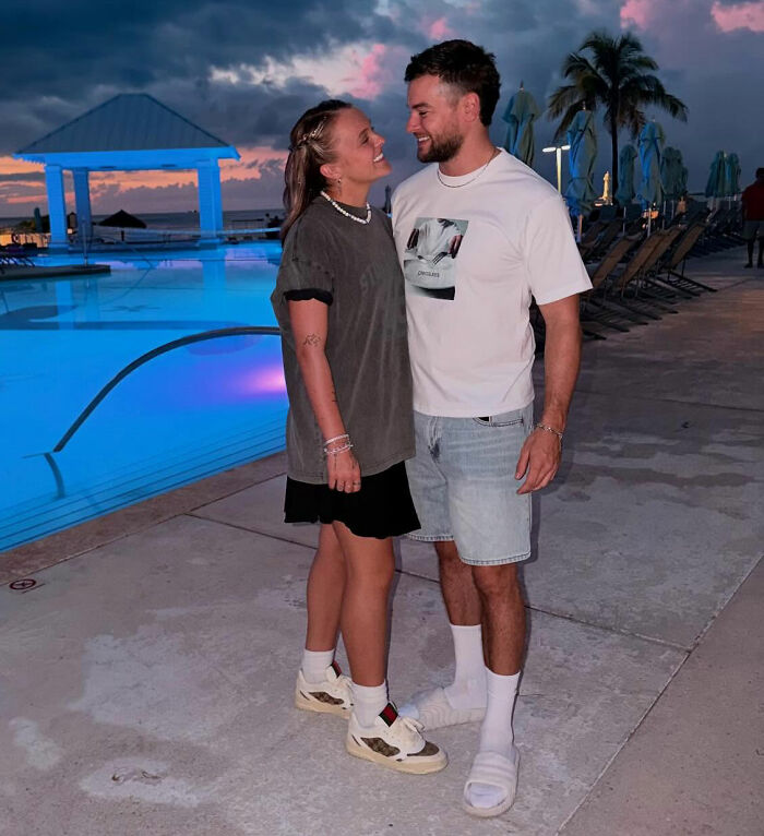 Chris Hughes and a woman smiling and standing near a pool at sunset, JoJo Siwa's fans stunned by reality TV confession.