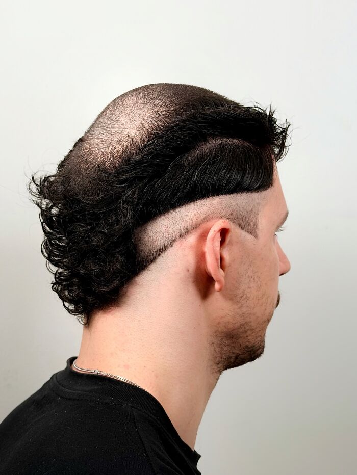 Man with bold barber haircut featuring shaved sides, a sharp part line, and styled curly hair on top smiling in a studio setting