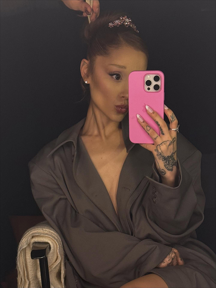 Ariana Grande taking a selfie wearing a dark oversized blazer, highlighting emotional age regression in recent fan reactions.