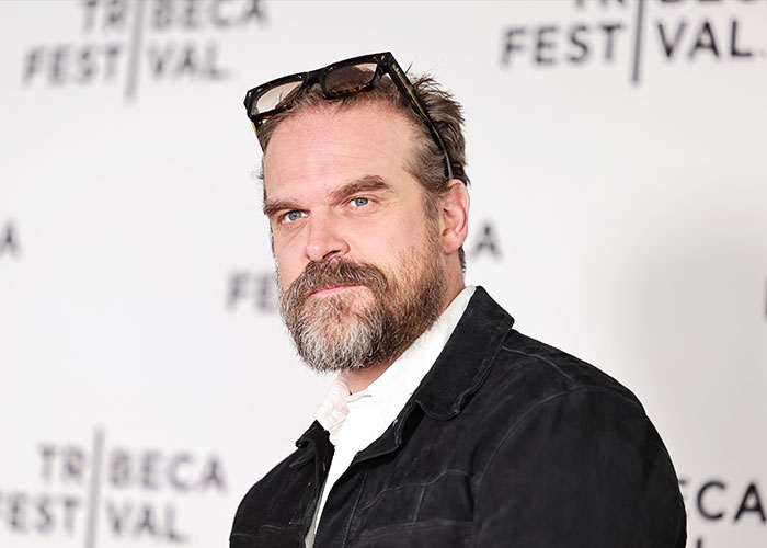 David Harbour at Tribeca Festival, wearing a black jacket and glasses on head, linked to Stranger Things co-star love admission.