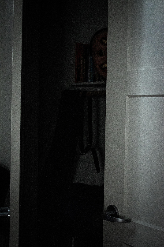 Dimly lit room with a partially open door revealing a creepy mask in the dark, evoking scary games to play with friends.