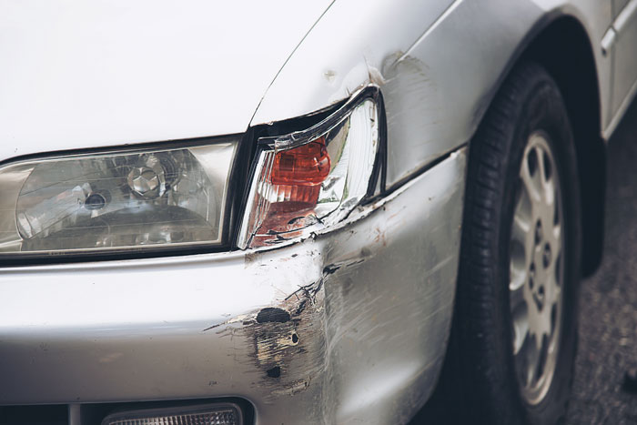 Silver car showing damage with scratches and dents on the front side, illustrating a moment of instant karma.