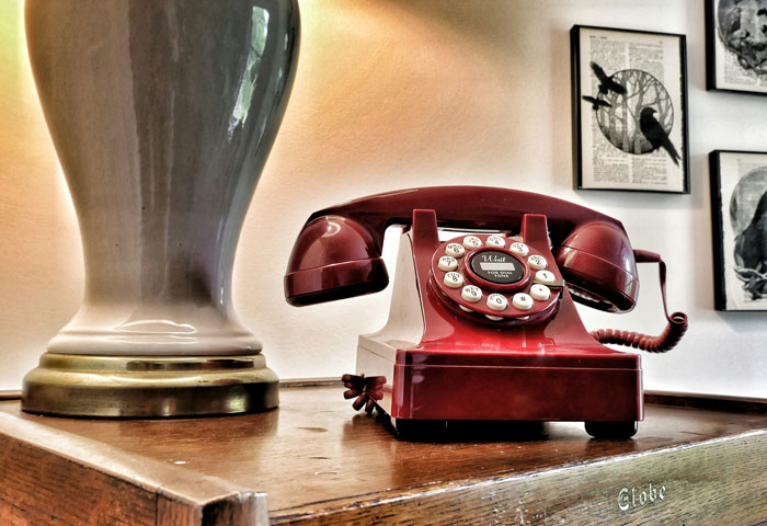 Vintage red rotary phone on wooden table next to lamp, illustrating an Oscar-worthy performance in deception stories.