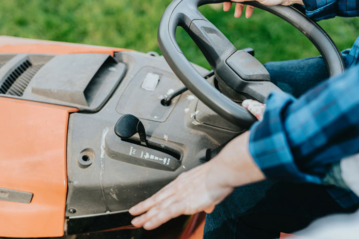 Person wearing blue plaid shirt operating a lawn tractor, illustrating funny patients comments breaking serious hospital vibe.