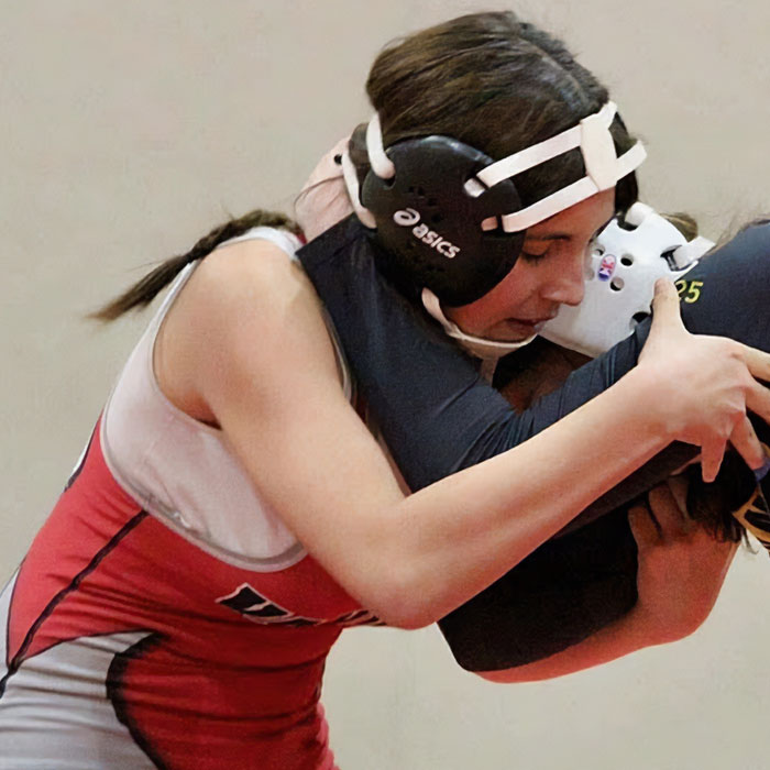 Teenage girl wrestling in a gym, wearing protective headgear and a red and white singlet during a match. Teenage girl wrestling in a gym, wearing protective headgear and a red and white singlet during a match.
