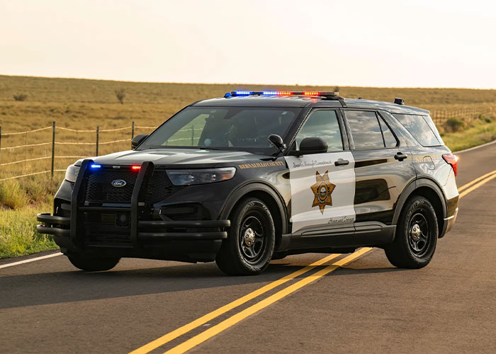 Police SUV with flashing lights parked on rural road during daylight, related to man accused in unusual m****r case.