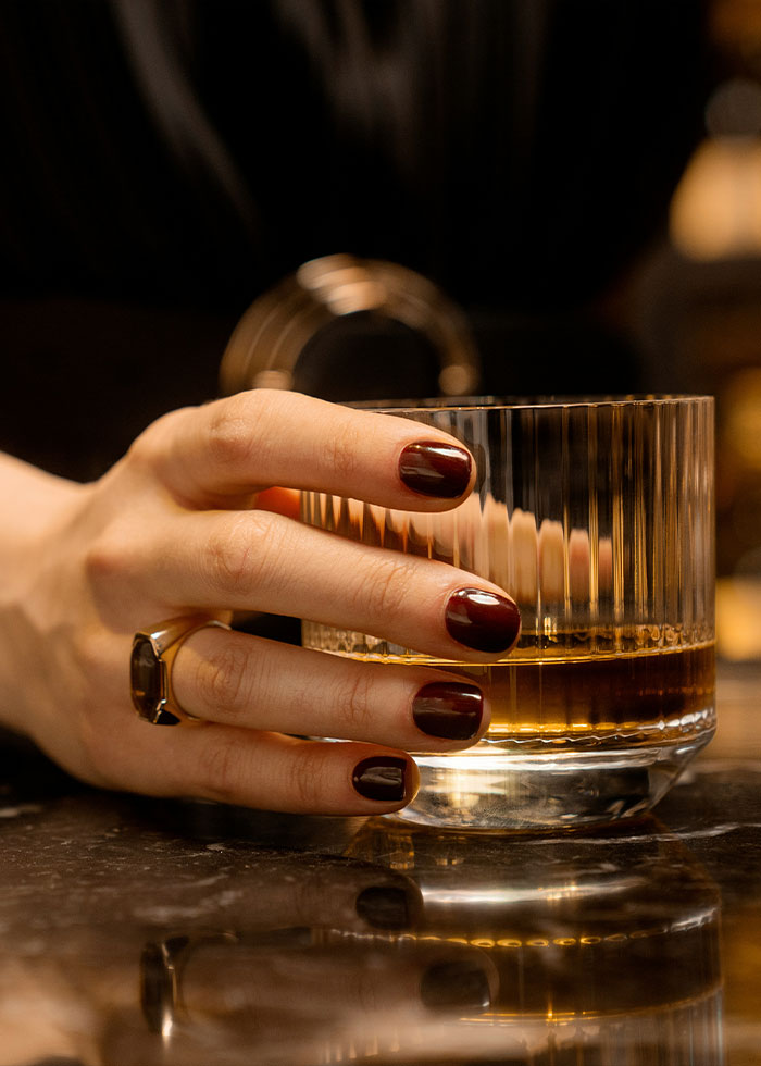 Hand with dark red nails and ring holding glass of whiskey, symbolizing red flags of a narcissist behavior. Hand with dark red nails and ring holding glass of whiskey, symbolizing red flags of a narcissist behavior.