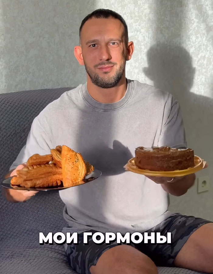 Fitness coach holding plates of pastries and cake during a binge-eating challenge involving mayo, seated indoors