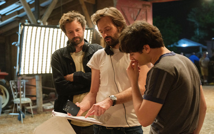 Three men discussing a script on set, highlighting challenges child actors face becoming adult actors in new performances. Three men discussing a script on set, highlighting challenges child actors face becoming adult actors in new performances.