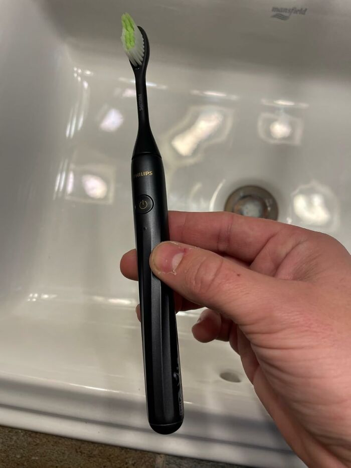 Hand holding black Philips electric toothbrush over a white sink, featured in Black Friday deals to add to your wishlist.