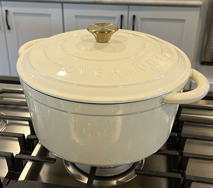 Cream-colored cast iron pot with gold k**b on stovetop, ideal aesthetic gift for kitchen decor and cooking lovers.