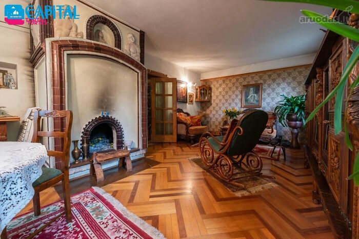 Vintage living room with wooden floor, fireplace, antique furniture, and decorative plants in wild real estate listing.
