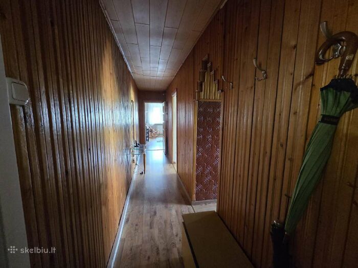 Narrow hallway with wood paneling and hardwood floor in a wild real estate listing considered unusual for selling properties.
