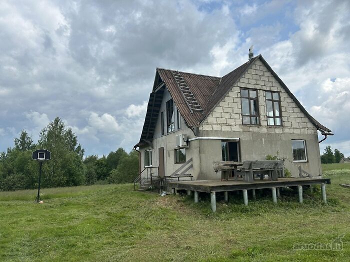 Unfinished house with an old roof and a basketball hoop on a large grassy plot, part of wild real estate listings.