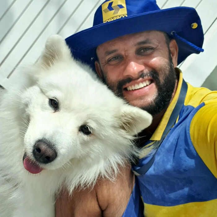 Mailman smiling and posing with a fluffy white dog, showing friendship on his delivery route.