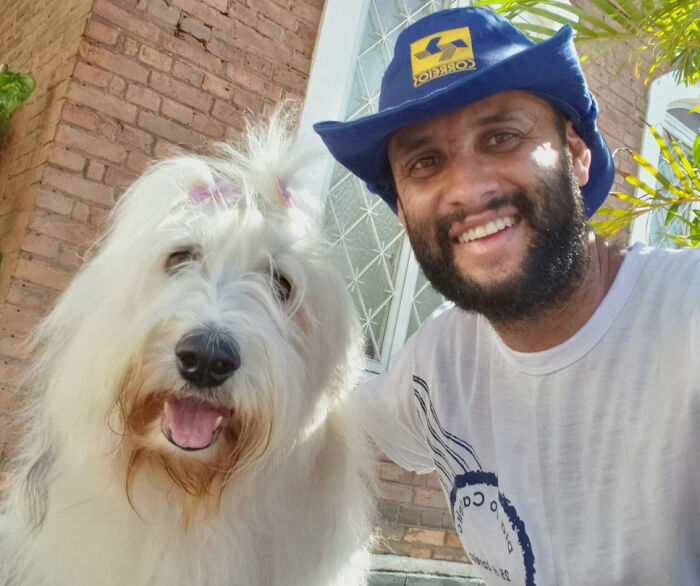 Mailman smiling with a fluffy white dog, showing the strong bond between the mailman and dogs on his route.