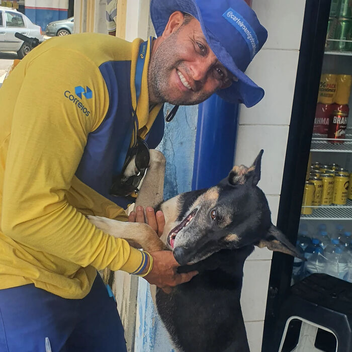 Mailman in yellow uniform happily hugging a black and tan dog, showing bond with dogs on his route.