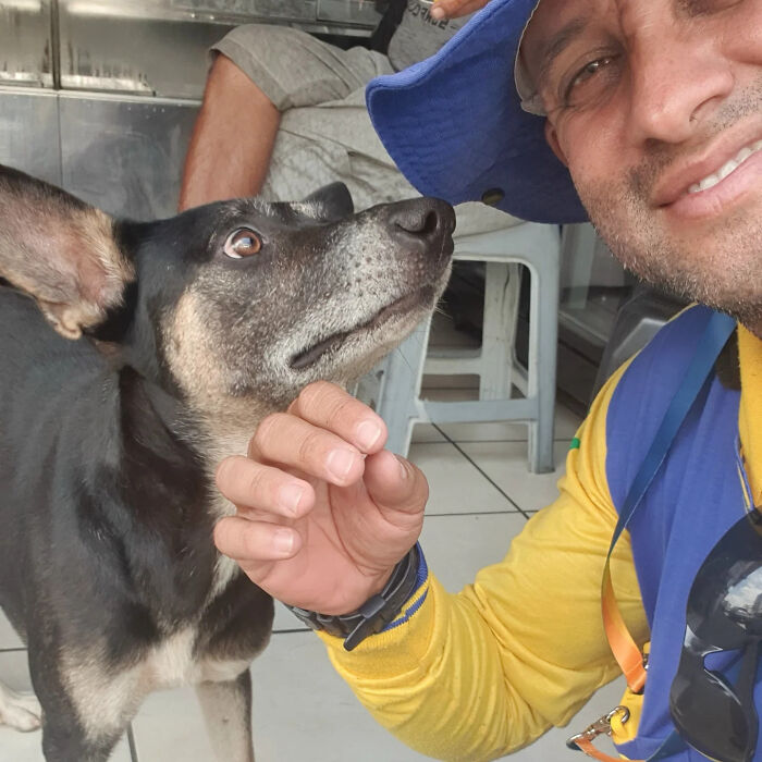 Mailman in yellow uniform happily hugging a black and tan dog, showing bond with dogs on his route.
