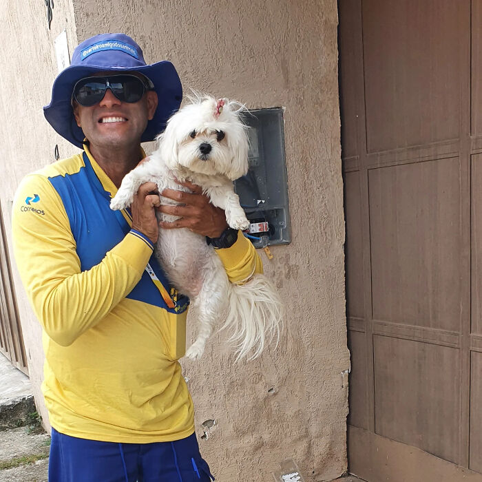Mailman smiling and holding a small white dog, showing the bond between mailman and dogs on his route.