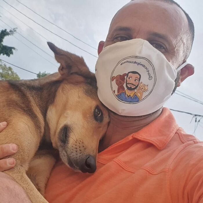 Mailman wearing mask hugging a dog close, showing a strong bond and friendship on his delivery route.