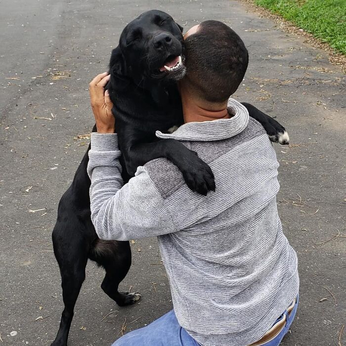 Mailman hugging a happy black dog on his route, showing the special bond between the mailman and every dog.