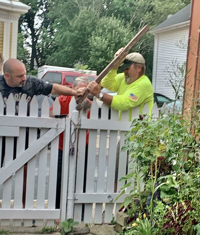 Two men helping each other fix a broken white fence gate, showing faith in humanity restored through kind gestures.