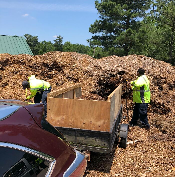 Two workers in safety vests filling a trailer with mulch, showcasing faith in humanity restored through kind actions.