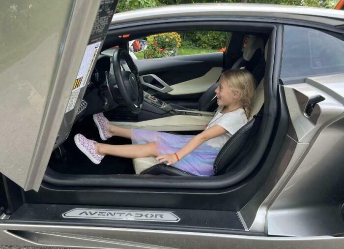 Young girl smiling while sitting in a luxury car, showing faith in humanity restored through small joyful moments.