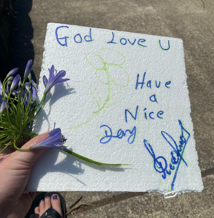 Hand holding a note saying God love you, Have a nice day, with purple flowers, spreading faith in humanity restored.