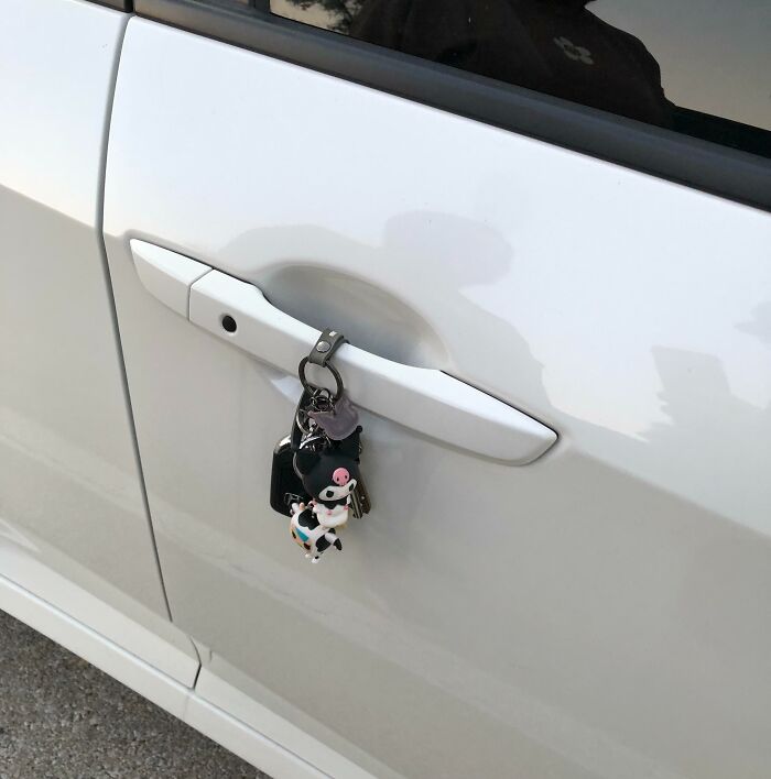 Keys with cartoon cow keychain left hanging on a white car door handle, faith in humanity restored moment.