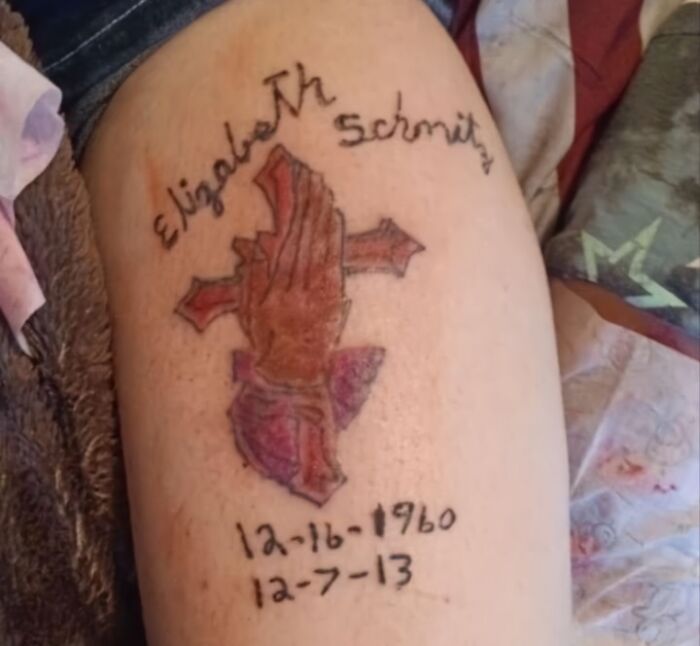 Tattoo of praying hands and a cross with a dated memorial and handwritten-style text on a person's thigh.
